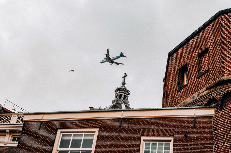 Airplane passing above brick buildings and church cupola in Amsterdam on a cloudy day.
