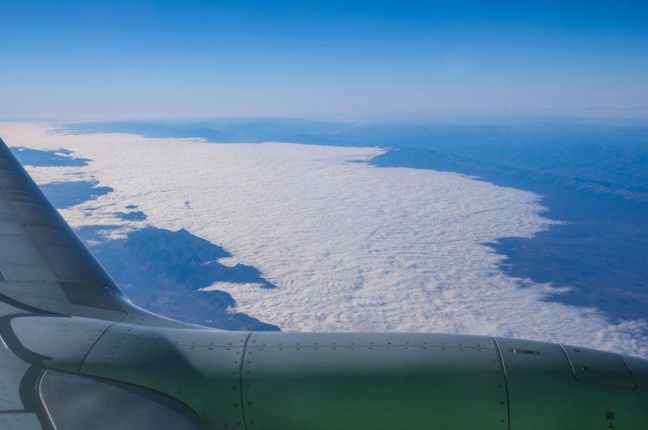 A stunning aerial view showing a snow-covered landscape with an aircraft wing against the blue sky.