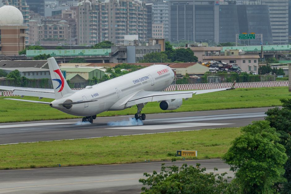 A China Eastern airplane landing on a runway with a city skyline in the background.