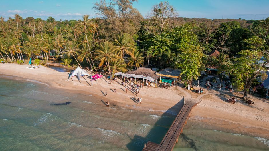 Stunning aerial shot of a vibrant tropical beach with palm trees and a wooden pier in Ko Mak, Thailand.