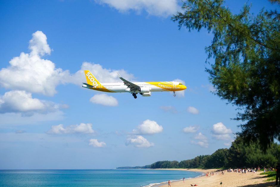 Commercial airplane landing over a beautiful beach in Phuket, Thailand with clear skies.